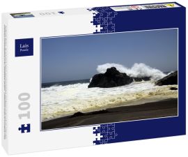 Lais Puzzle - Kraftvolle Wellen, die auf einem Felsen zusammenstoßen und Wasser in der Luft am entfernten schwarzen Lavasandstrand an der Pazifikküste spritzen - Cobquecura Piedra De La Loberia, Chile  - 100 Teile