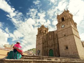 Lais Puzzle - Frau mit Keperina (Tasche auf dem Rücken) auf den Stufen der Kathedrale von Puno (Peru) sitzend - 500 & 1.000 Teile