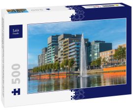 Lais Puzzle - Lelystad: Einheimische gehen und überqueren den Teich mit Brunnen in der Mitte mit modernen Geschäftsgebäuden und Häusern im Hintergrund - 500 Teile