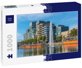 Lais Puzzle - Lelystad: Einheimische gehen und überqueren den Teich mit Brunnen in der Mitte mit modernen Geschäftsgebäuden und Häusern im Hintergrund - 1.000 Teile