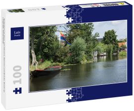 Lais Puzzle - Ruderboot im Fluss, mit Häusern, Bäumen und Brücke. Broek op Langedijk, Niederlande - 100 Teile